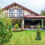 Exterior of contemporary residential house with balcony and cozy terrace with couch near trees on green yard on daytime